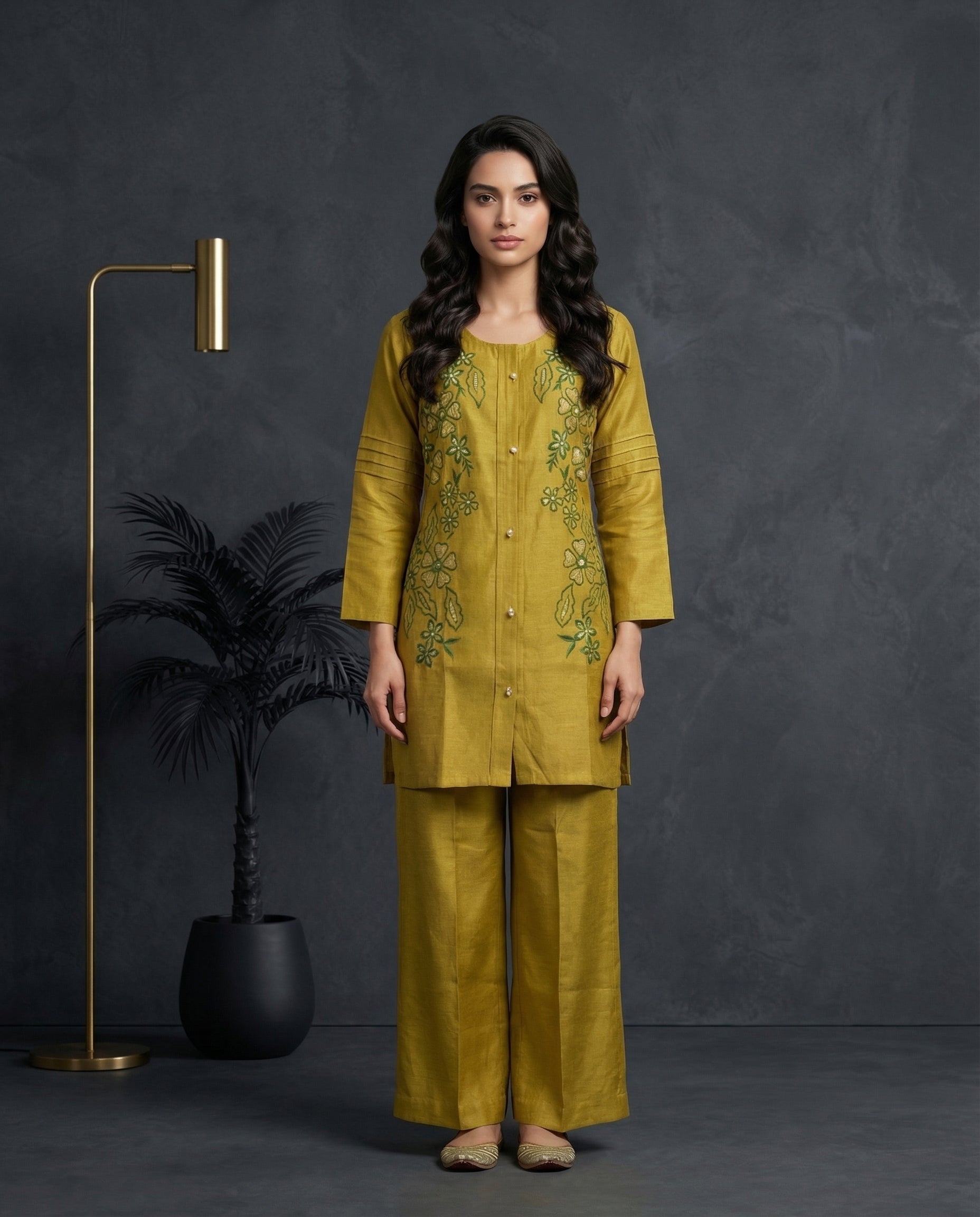 Woman wearing a mustard yellow embroidered outfit standing against a dark background with decorative elements.